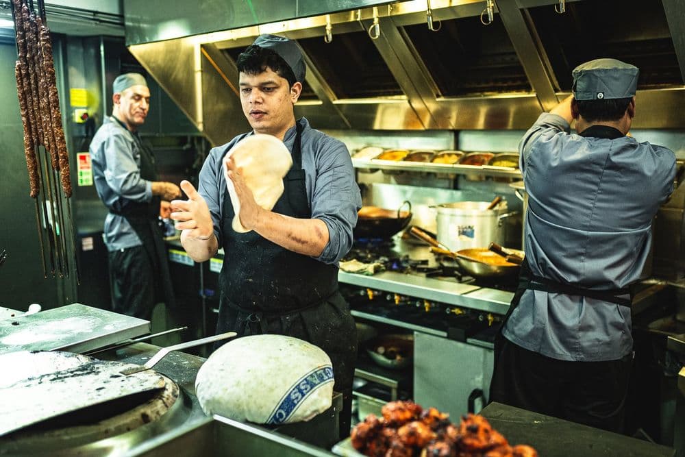 A chef stretching naan dough in the open kitchen